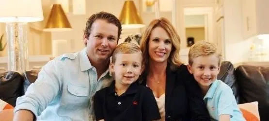 The image shows a family posing together on a couch, with a man, woman, and two young boys smiling towards the camera.