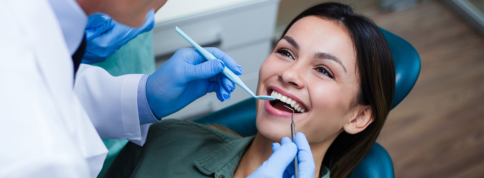 A person receiving dental care with a dentist performing the procedure, both wearing medical attire.