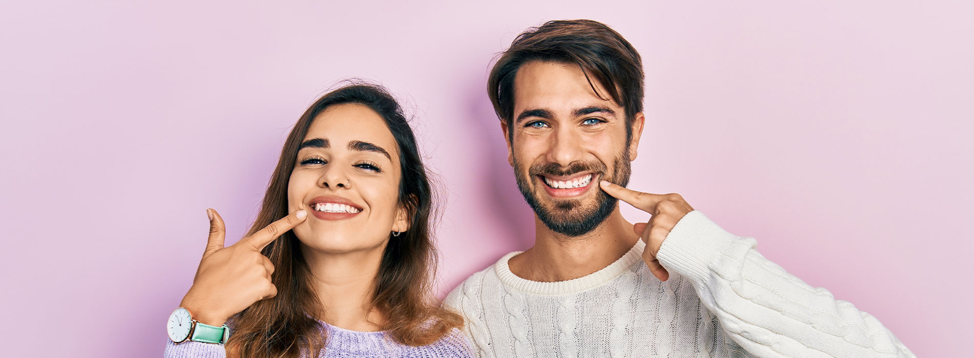 Two people posing with playful expressions  man pointing at his teeth, woman smiling broadly.
