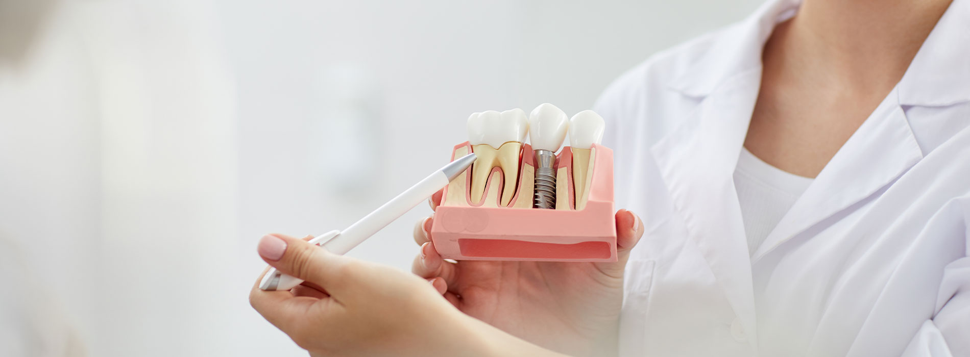 The image shows a person holding an open red box with two small white objects inside, which appear to be toothbrushes, against a blurred background that suggests a clinical or medical setting.
