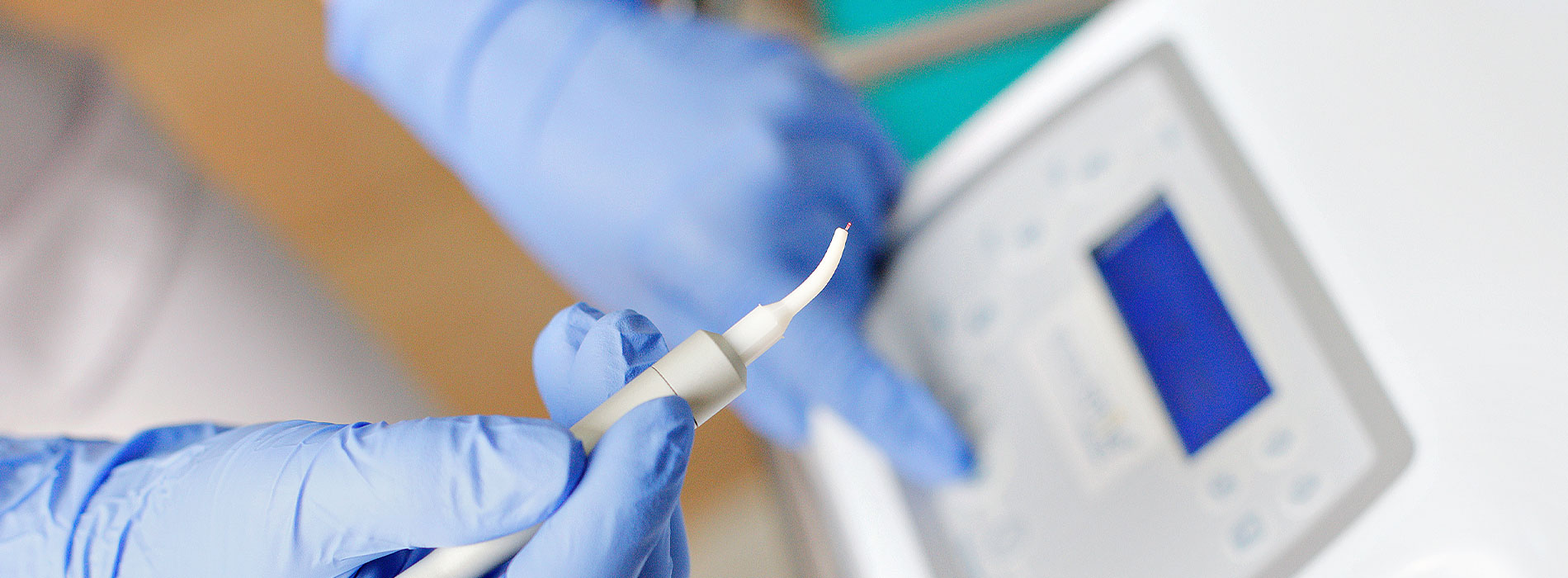 The image shows a close-up view of a person s hands wearing blue gloves, holding a white object with a clear substance inside, which appears to be a lab test tube, against a blurred background that includes a table and a chair.
