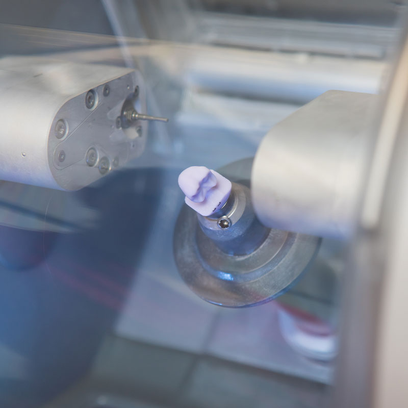 The image shows a close-up view of a machine with various components, including a cylindrical object with a circular opening at one end and a small protrusion on top, which appears to be a part of the manufacturing process.