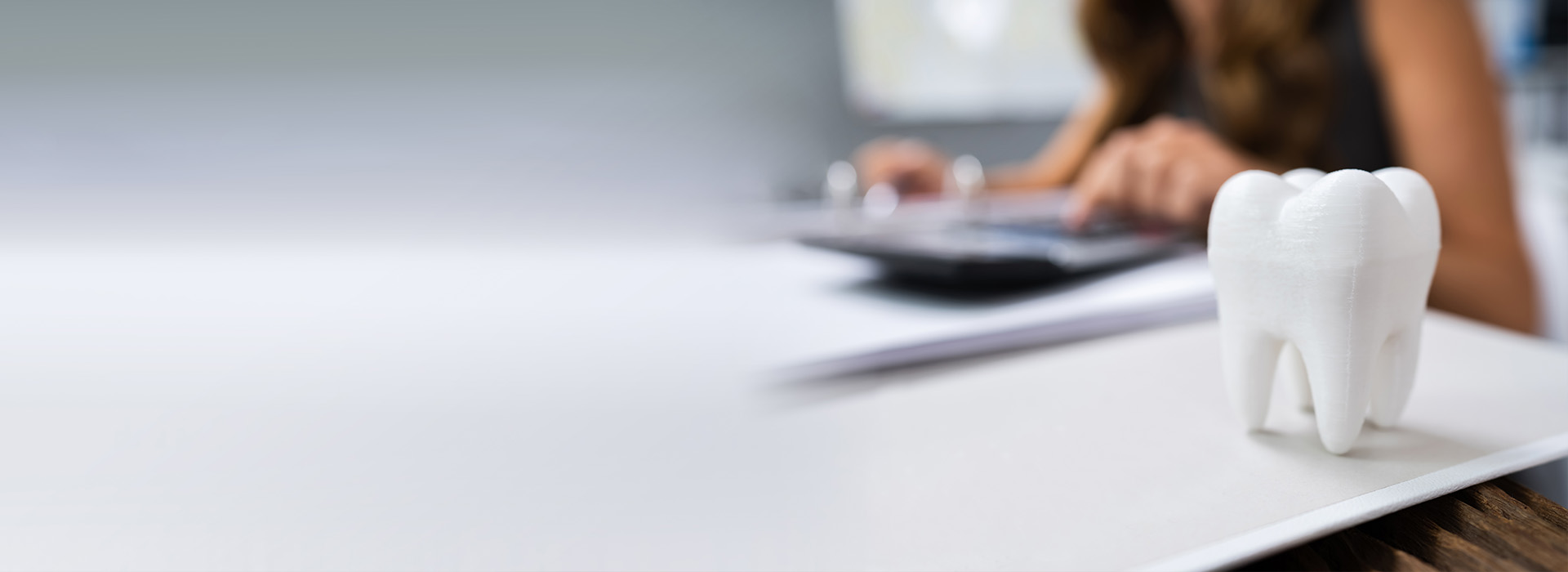 The image shows a person sitting at a desk with a computer and a toothbrush holder, which contains a toothbrush, set against a blurred background.