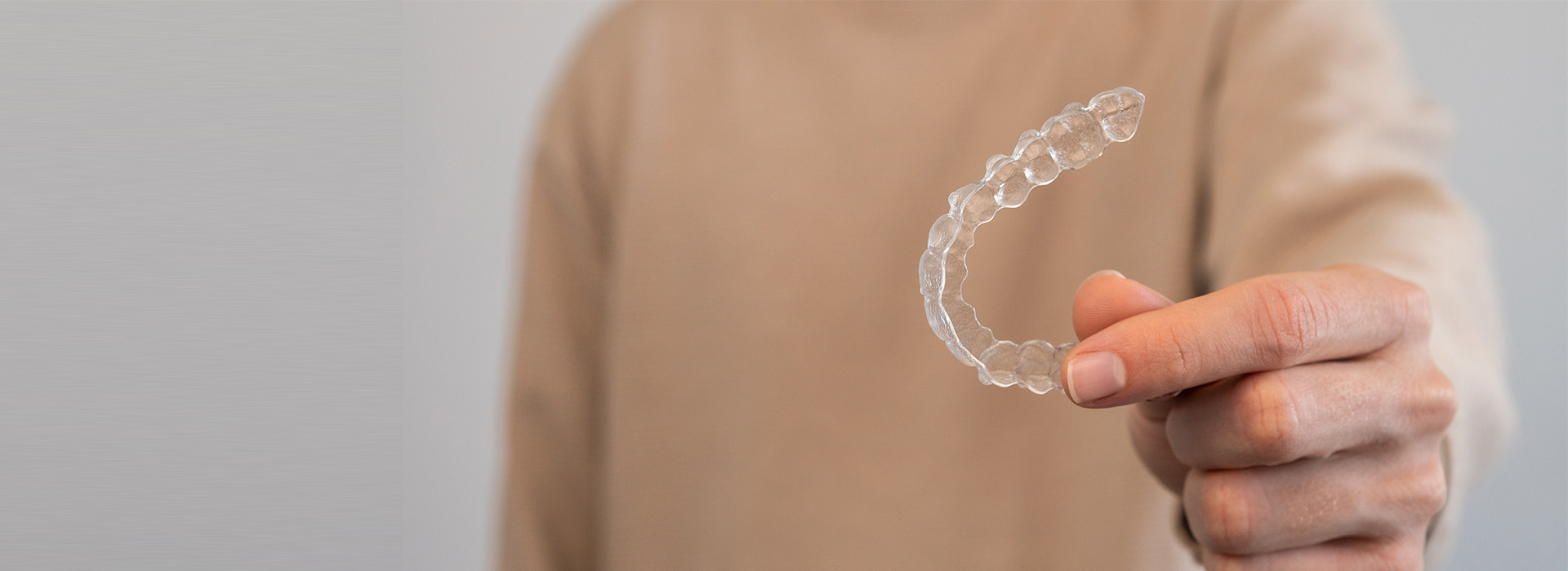 The image shows a person s hand holding a transparent object with a hollow center, resembling a plastic ring or a piece of plastic with an opening, against a blurred background.