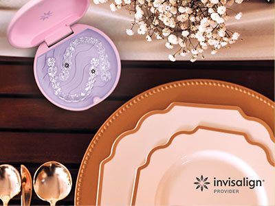 The image shows a table setting with various dinnerware items such as plates, bowls, and spoons arranged on a wooden surface, along with a decorative piece resembling a seahorse-shaped object with an open lid, and a watermark for  Invisalign  in the lower right corner.