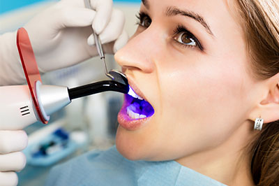 The image shows a person receiving dental care with a focus on a specialized device being used by the practitioner.