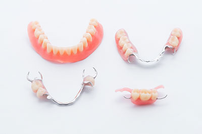 The image displays a collection of dental appliances, including a set of false teeth with pink gums and metal clasps for attachment, arranged on a white background.