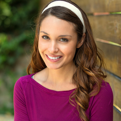 A woman with long hair, wearing a headband and a purple top, smiling at the camera.