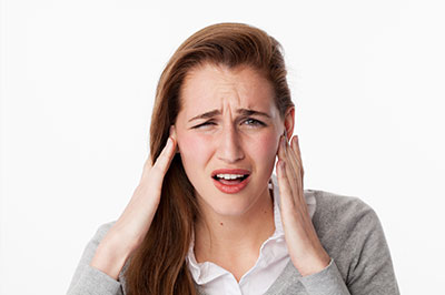 The image shows a woman with her hand on her head and her mouth open, displaying an expression of discomfort or pain.