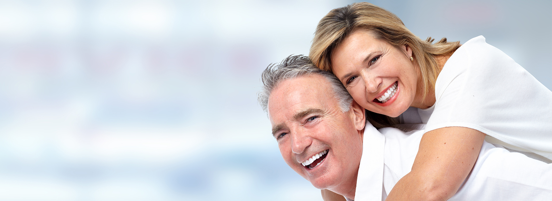 The image shows a man and a woman smiling and embracing each other while standing outdoors with a blurred background, suggesting a happy moment between them.