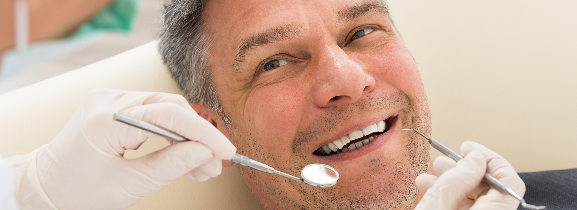 A man receiving dental care with a smiling expression while holding a toothbrush.