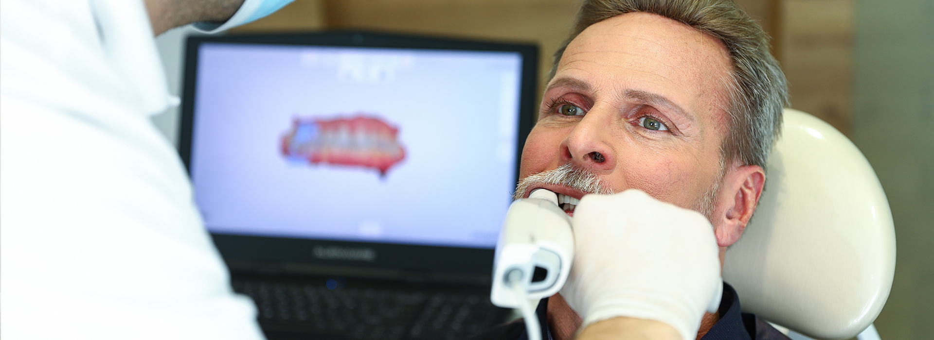 A man receiving dental care with a visible computer screen displaying medical images.