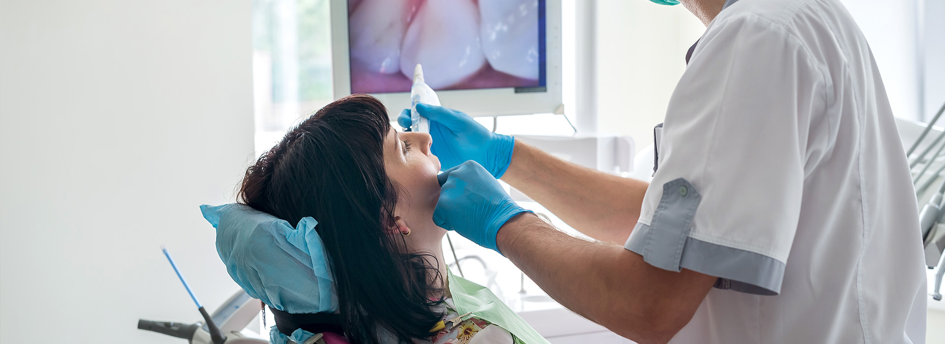 The image depicts a dental professional attending to a patient s teeth during a dental appointment, with the patient seated in a chair and wearing protective eyewear.