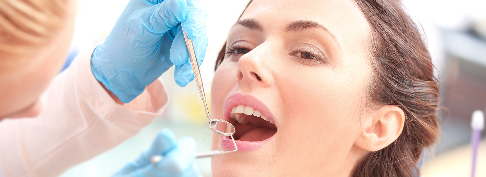 The image shows a woman receiving dental treatment with a syringe being held by a person wearing blue gloves, while she looks onwardly.