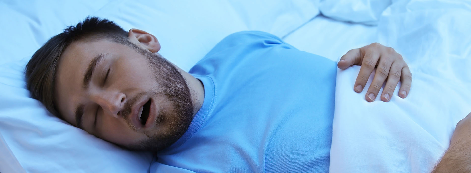 The image depicts a man lying down on a bed with his eyes closed, appearing to be asleep or resting.
