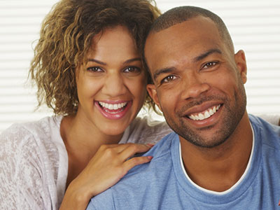 A man and woman smiling together, with the man wearing a blue shirt and the woman in a white top.