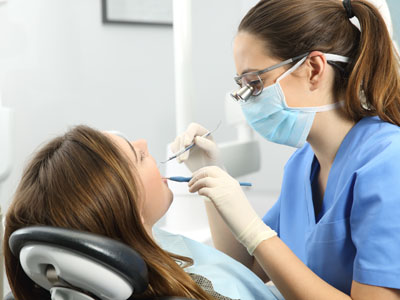 A photograph of a dentist performing a procedure on a seated patient while wearing protective gear.