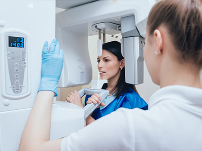 A woman stands in front of a 3D scanner machine while a man in protective white gloves inspects the device, with both individuals wearing face masks.