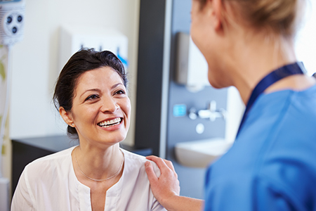 The image depicts two individuals, one of whom appears to be a woman with a smile, possibly engaging in a conversation or interaction, within a medical setting, likely a hospital or clinic.