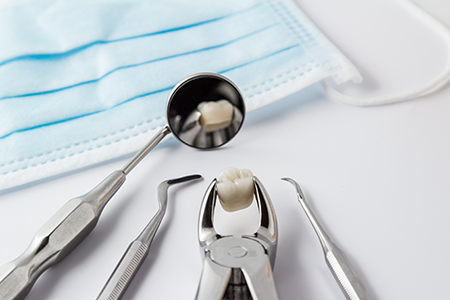 The image shows a dental tool with a tooth placed inside it, set against a backdrop of a blue surgical mask and dental instruments, possibly indicating a dental cleaning or examination process.