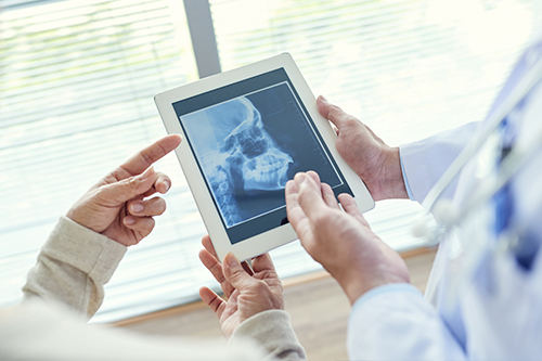 The image shows two individuals viewing a tablet screen with an X-ray image displayed on it  the setting appears to be a medical office, indicated by the presence of a medical professional.