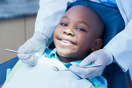 A young boy sitting in a dental chair at a dentist s office, smiling broadly while wearing protective eyewear and receiving dental care.