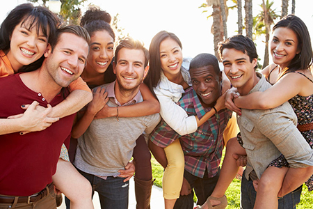 The image depicts a group of young adults posing together outdoors during daylight, with a cheerful atmosphere and clear skies.