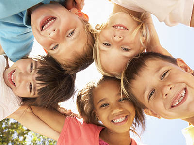 A group of six children with different expressions are huddled together, smiling and looking at the camera.