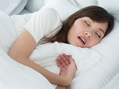 A woman sleeping peacefully in bed with her eyes closed, wearing a white shirt and her mouth open slightly.