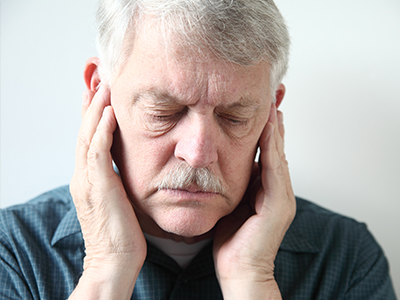 The image shows a man with his hands on his ears, appearing to be experiencing discomfort or pain.