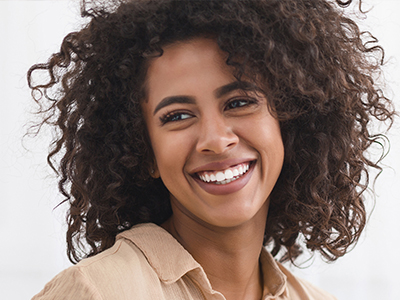 A woman with curly hair, smiling, wearing a light-colored top.